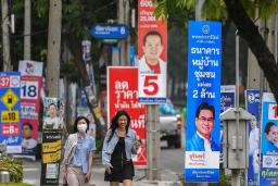 　タイ下院総選挙のポスターが並ぶバンコクの通りを歩く人たち＝４月２６日（ロイター＝共同）