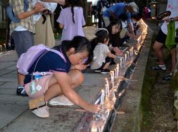 　高野山の奥の院で開かれた「ろうそくまつり」で、ろうそくに火をともす子どもら＝１３日夕、和歌山県高野町