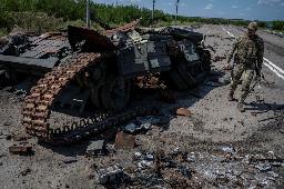 　ウクライナ南部ザポロジエ州ロボティネ近くで破壊された戦車の横を歩くウクライナ兵＝２５日（ロイター＝共同）