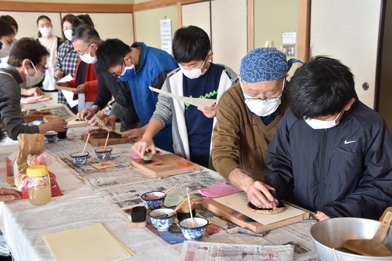 江戸木版画摺師（すりし）の松崎さん（右から２人目）から多色刷りのこつを教わる児童＝鋸南町立中央公民館
