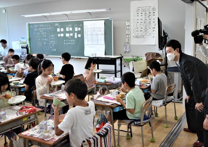 机の間隔を空けて工夫した対面方式での給食の様子を視察する熊谷知事（右）＝３０日、習志野市立谷津小
