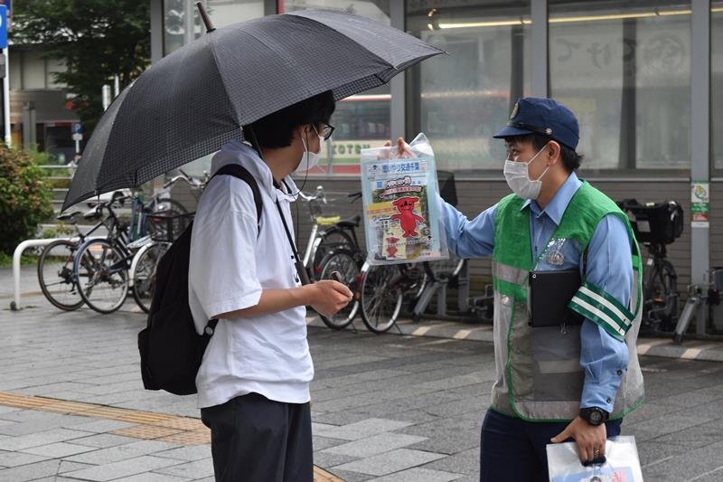 啓発グッズを配り、自転車の安全利用を呼びかける警察官＝１５日午後、千葉市中央区のＪＲ千葉駅前
