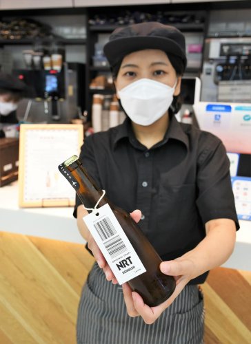 バゲージタグを付けたデザインの成田空港エールを紹介するカフェスタッフ＝成田空港
