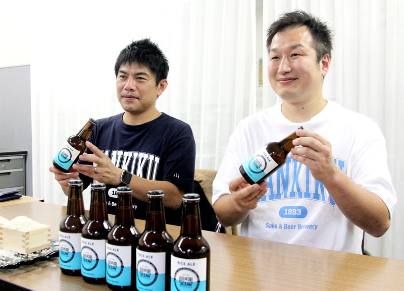 「ワールドビールアワーズ２０２２」ライスビール部門最高賞に輝いた「クジュウクリオーシャン・ライスエール」を見せる佐瀬代表（写真左）と風間さん＝千葉市中央区
