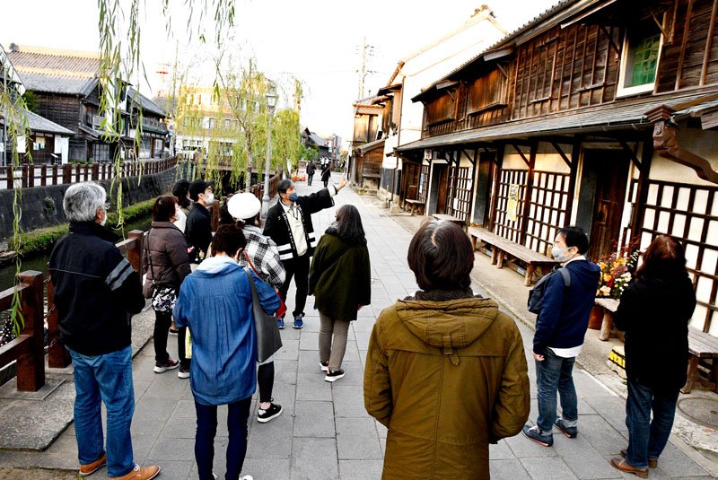 歴史的建造物が立ち並ぶ佐原の町並みの案内を聞く参加者ら＝香取市
