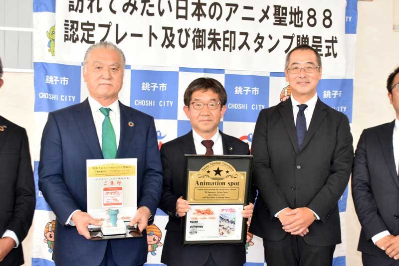鈴木専務理事（右）から受け取ったプレートと御朱印スタンプを手にする越川信一市長（中央）と市観光協会の赤坂修会長＝銚子市役所