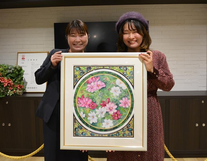 コスモスを色鮮やかに愛らしく描いた作品を寄贈したＮＡＯさん（右）。左は矢部支店長＝八千代市
