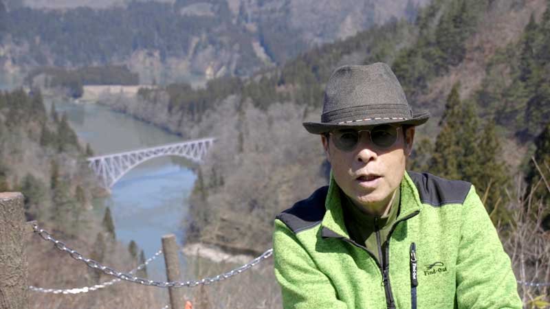 映画「霧幻鉄道　只見線を３００日撮る男」の一場面。ＪＲ只見線の橋を後方に語る星賢孝さん（ミルフィルム提供）
