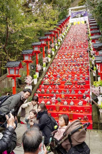 遠見岬神社の石段６０段に飾られたひな人形約１８００体の前で写真を撮る親子連れら＝２４日、勝浦市