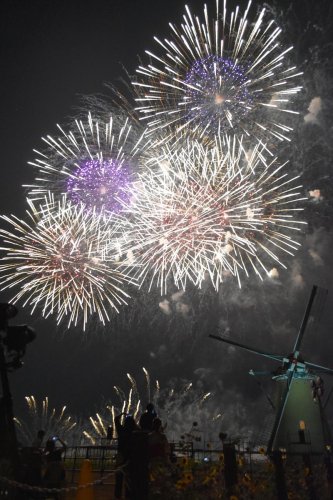 印旛沼沿いの佐倉花火フェスタで、風車と共演する大輪の花火＝５日夜、佐倉市
