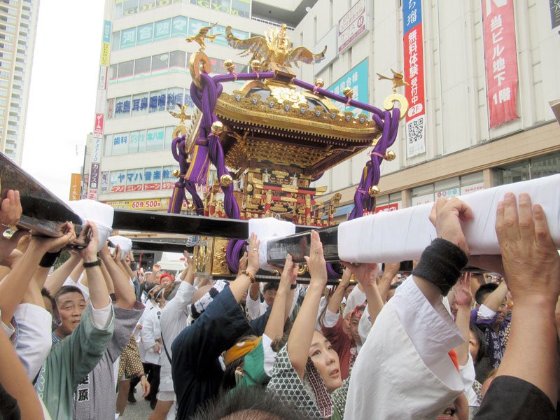 ＪＲ本八幡駅前で、大みこしを掲げる担ぎ手たち＝１日、市川市