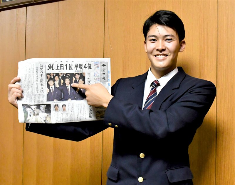 ドラフト会議翌日の新聞を手に、笑顔の幕張総合高の早坂＝１０月３０日、千葉市美浜区