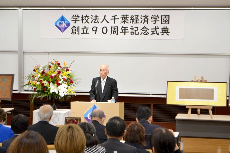 創立９０周年記念式典であいさつする佐久間理事長＝１５日、千葉市稲毛区の千葉経済学園