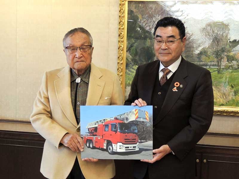 ４０メートルはしご付き消防車の寄付目録贈呈式に臨んだ根本さん（左）と鈴木市長。写真と同規格の消防車が市に寄贈される＝３０日、野田市
