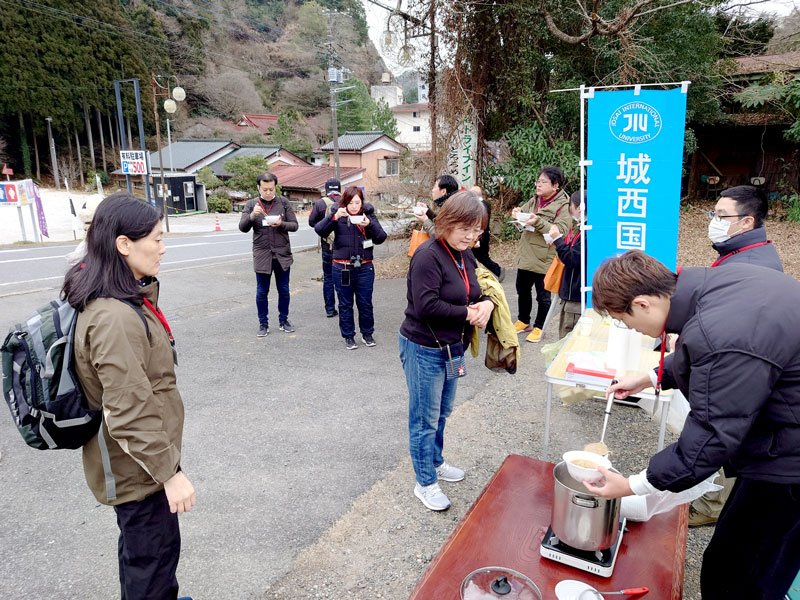 ハイキング参加者に、しし鍋汁を振る舞う城西国際大の学生（右）＝市原市戸面