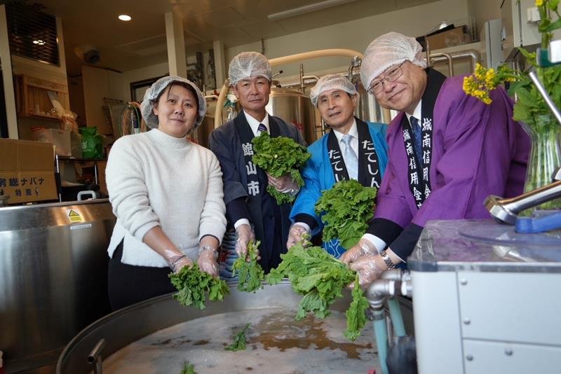 菜の花を醸造機に入れる川本理事長（右）ら＝東京都
