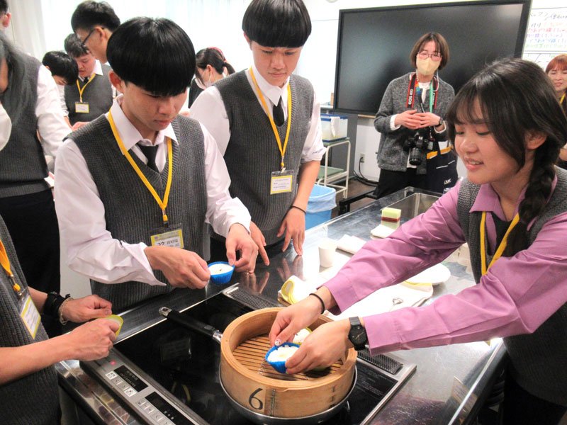 千葉商科大生の指導を受けて「生米の蒸しパン」作りに取り組む台湾の高校生ら＝市川市