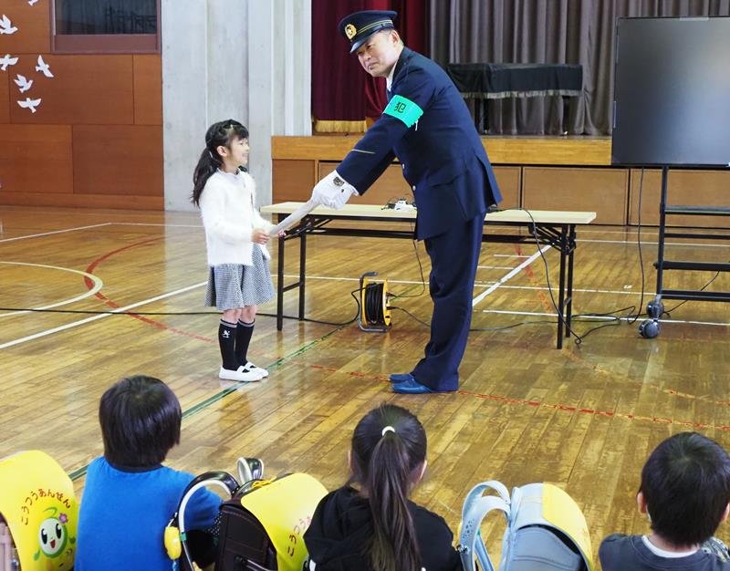 庄村署長（右）から防犯グッズを受け取る新１年生＝富津市
