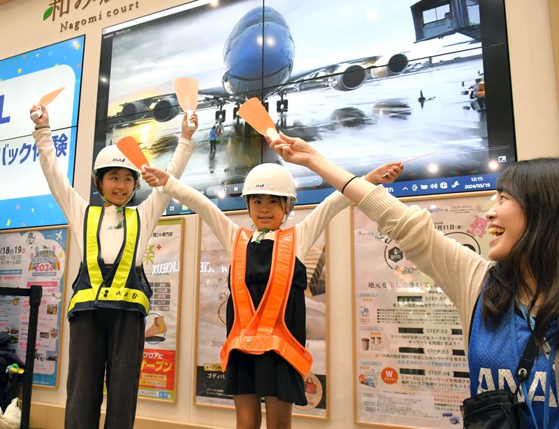 スタッフ（右）に教わり、駐機する航空機の誘導を疑似体験する子どもたち＝１９日、成田市