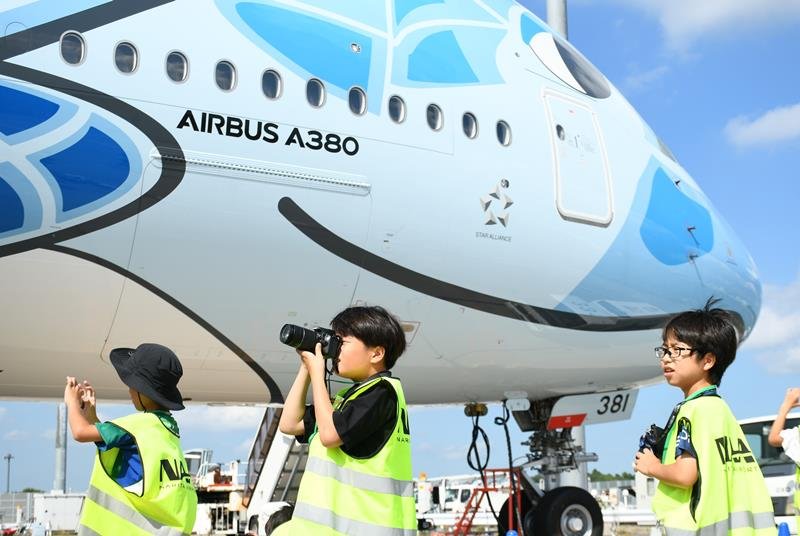 ウミガメが描かれた大型機「フライングホヌ」に近づいて撮影を楽しむ小学生たち＝成田市
