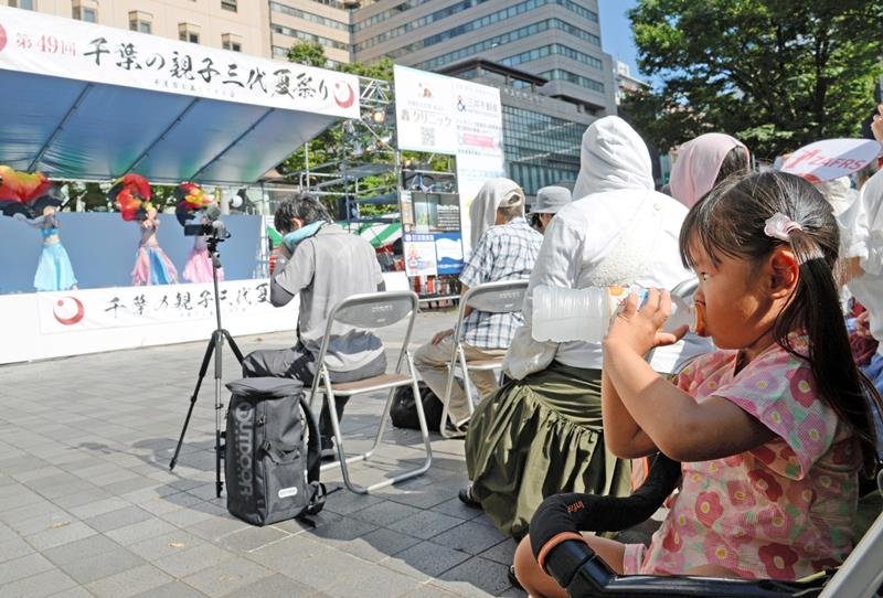 強い日差しが照り付ける「千葉の親子三代夏祭り」のダンスステージ会場で、凍らせたペットボトルのドリンクを口にする女児＝１７日午後、千葉市中央区の中央公園