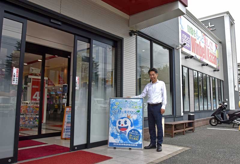 「酷暑避難場所」の目印となる看板を手に利用を呼びかける田中店長＝船橋市