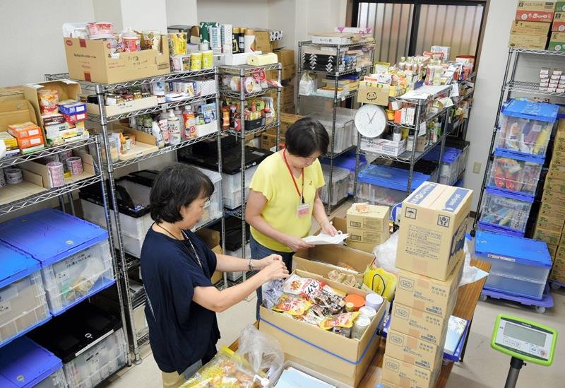 支援先に送る箱に食品を詰める「フードバンクふなばし」のスタッフ。潤沢にあるように見えるが、レトルトカレーなどは不足気味（写真下）。これまでは、ボックスがいっぱいになるほど集まっていたという＝船橋市
