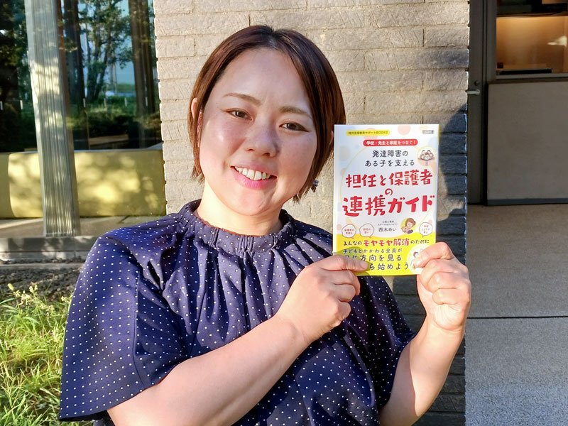 「発達障害のある子を支える　担任と保護者の連携ガイド」を手にする西木さん。