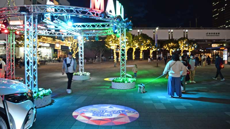 「マクハリイルミ」のイベントに初登場したオブジェ「レインボーサークル」。樹木を装飾した光るオーナメントなどイルミネーションを楽しむ市民ら＝９日、ＪＲ海浜幕張駅前