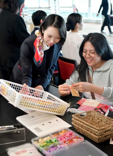 水引を装飾したスーツケースタグの制作体験を楽しむ旅客（右）＝成田市の成田空港