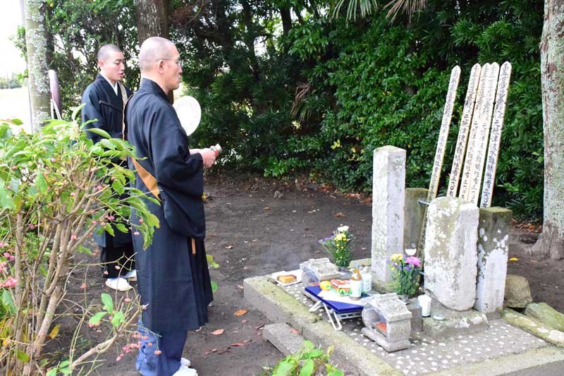 元禄津波の犠牲者を埋葬したと伝わる「無縁塚津波精霊様」の供養碑の前で読経する三橋住職（手前）ら＝２３日、白子町