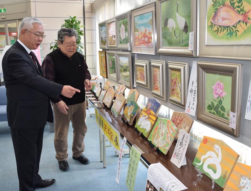来年の干支、巳の絵馬（右下）などを観賞する房総信用組合の三谷理事長（左）と作品を説明する矢部さん＝茂原市
