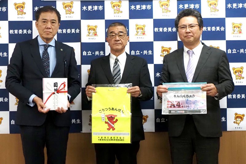 黄色いランドセルカバーなどを寄付する交通安全協会の竹内会長（中央）と安管協の大里代表理事（右端）＝木更津市