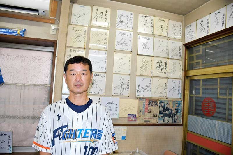 日ハムゆかりの選手らのサイン色紙が並ぶ「東新軒」店内と、店主の新川さん＝鎌ケ谷市