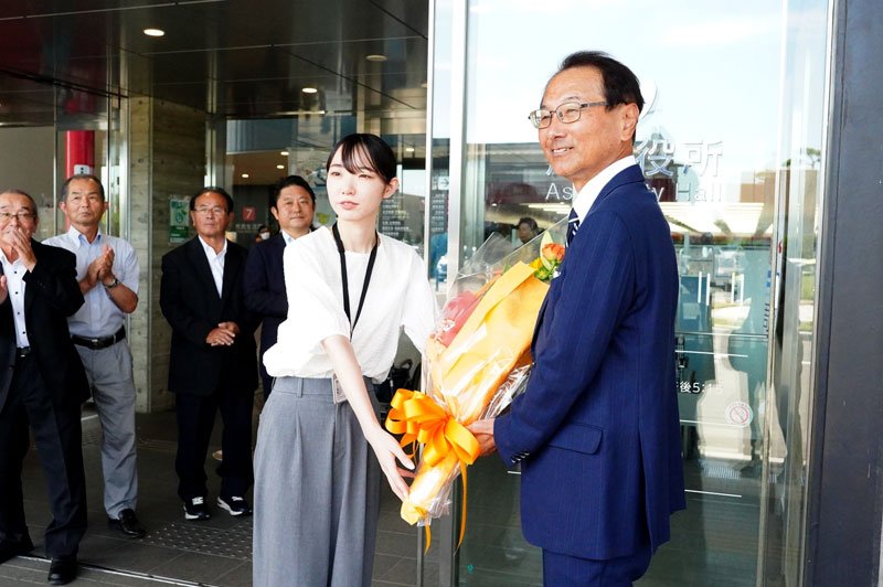 市役所玄関前で花束を受け取る米本市長（右）。実質的に２期目のスタートを切った＝２２日、旭市役所