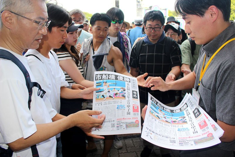 市船橋の優勝を速報した千葉日報号外に手を伸ばす高校野球ファンの観客＝２７日、ＺＯＺＯマリンスタジアム前
