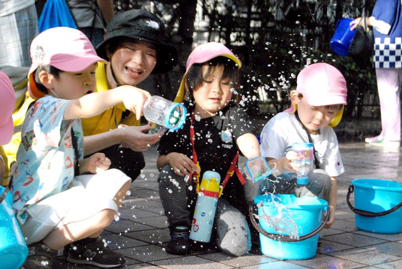 県内で暑さが続く中、地球や生活の環境変化を考える「打ち水」が行われ、園児らが自作したひしゃくで元気よく水をまいた＝２０日午後４時半ごろ、千葉市中央区新町　