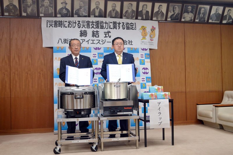 災害時の支援協力に関する協定を締結した北村市長（左）と中田社長。手前は寄贈された炊き出し用コンロとアイラップ＝八街市役所