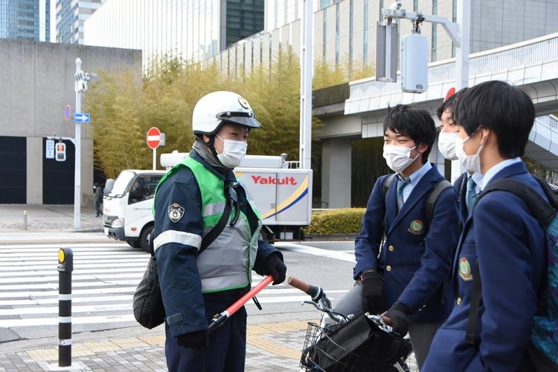 高校生に自転車乗車中のヘルメット着用を呼びかける警察官＝２０２３年２月、千葉市美浜区
