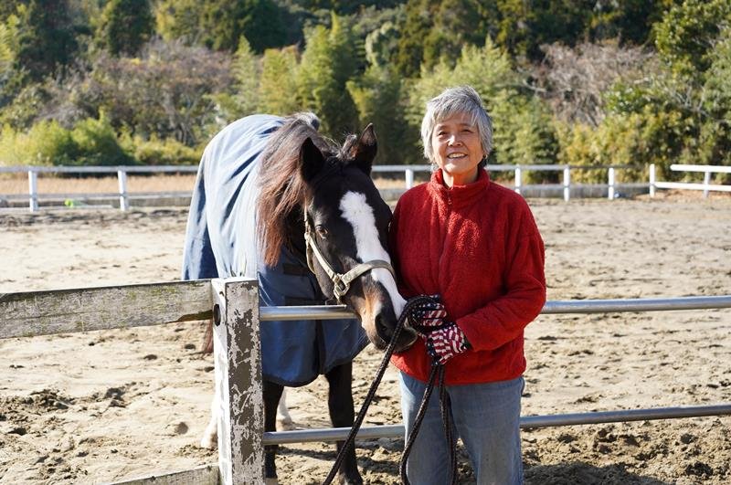 「夏は涼しい風が吹き抜ける」という高台の牧場で愛馬と共に笑顔を見せる市川粧子さん＝勝浦市
