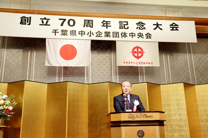 記念大会であいさつする飯塚会長＝２３日、千葉市美浜区