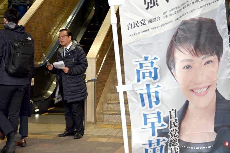 早朝から駅前でビラ配りを続けた自民元職の渡辺氏。高市首相ののぼりを置き、関係性をアピールした＝１月２６日午前、松戸市