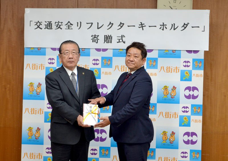 リフレクターを寄贈する全日本ロータス同友会千葉県支部の都築正茂支部長（右）＝八街市役所