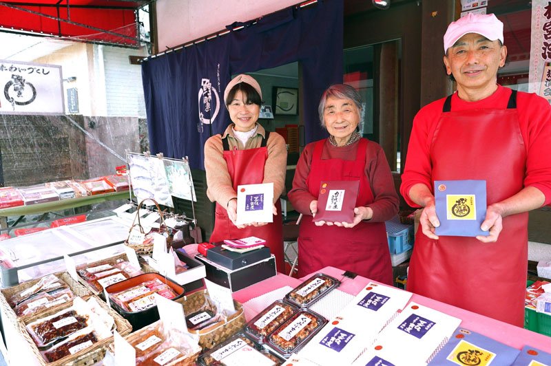 店の前でこだわりの商品を手に笑顔を見せる佃煮近江の岩成さん（右）と家族＝勝浦市