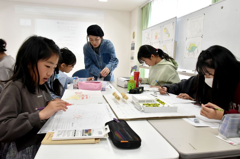 ヒラタシノさん（奥）からアドバイスを受けながら壁画のデザイン案を描く児童ら＝千葉市美浜区
