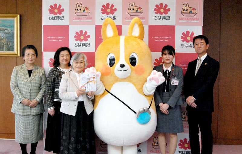 寄付金の贈呈式で、ちばコーギーを囲む千葉興銀、ちばこどもおうえんだんの担当者ら＝２１日、千葉市美浜区の同行本店