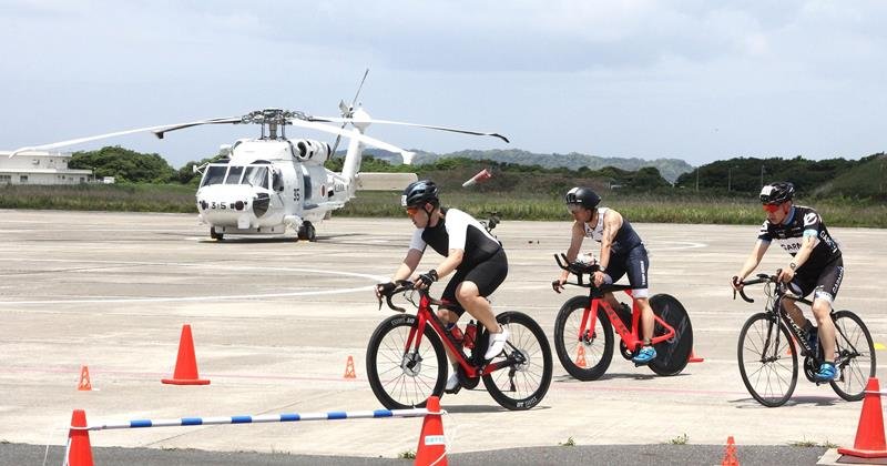 海上自衛隊館山航空基地内のヘリコプターを横目にバイクで疾走する選手たち＝２４日、館山市

