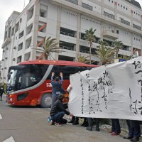 帰宅する邦人を乗せたバスを横断幕を掲げて見送る市民ら＝２月１３日、勝浦市墨名