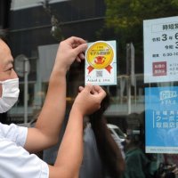 認証を受け、ステッカーを店の入り口に貼り付ける浅野店長＝２２日、千葉市中央区