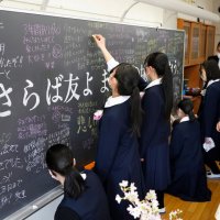 黒板に寄せ書きする卒業生